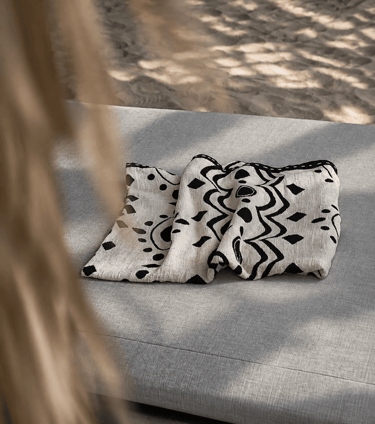 Folded black and cream KIND throw on a sunlit daybed