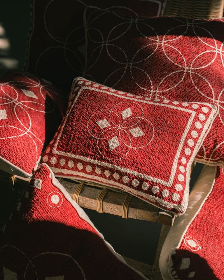 Red KIND cushions with cream circle and diamond prints on a wooden chair