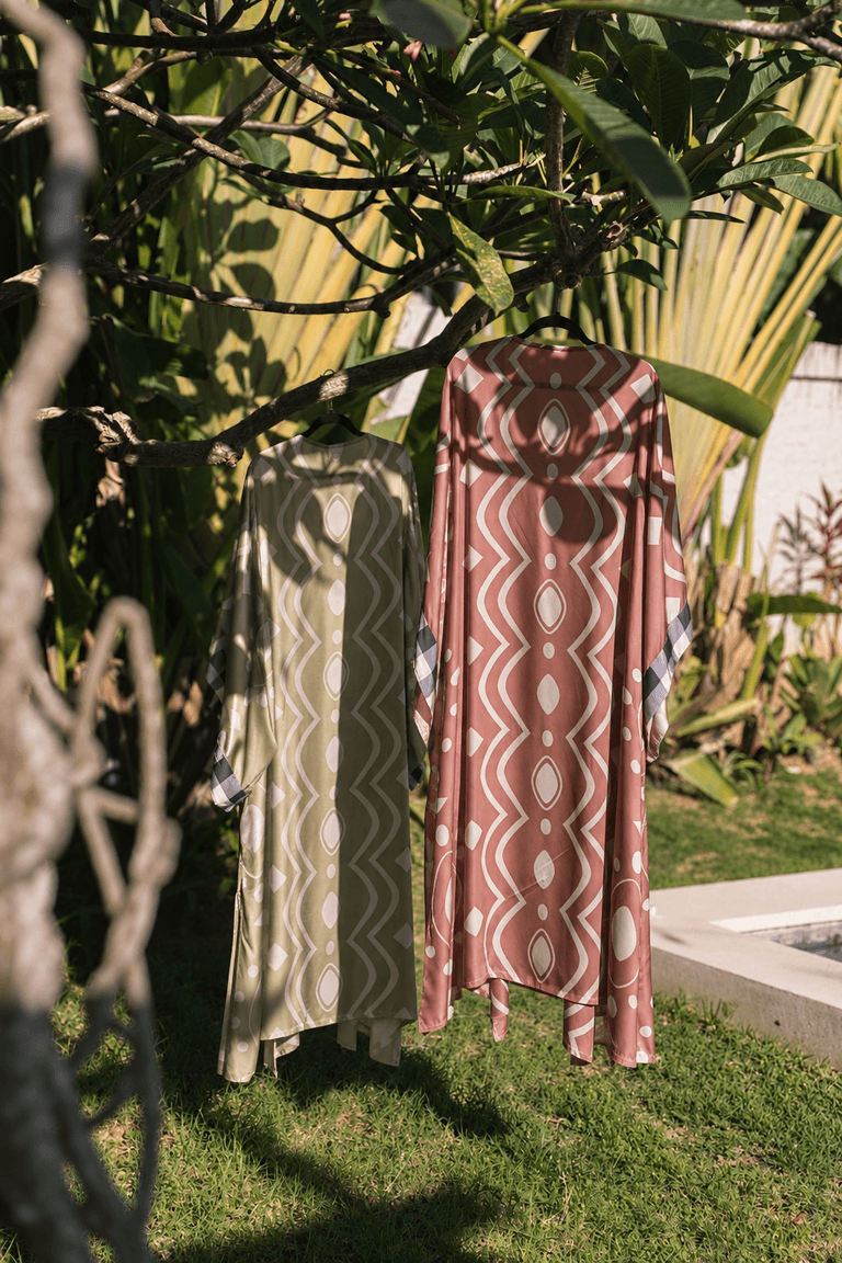 Two KIND kimonos in sage and terracotta prints hanging from a frangipani tree